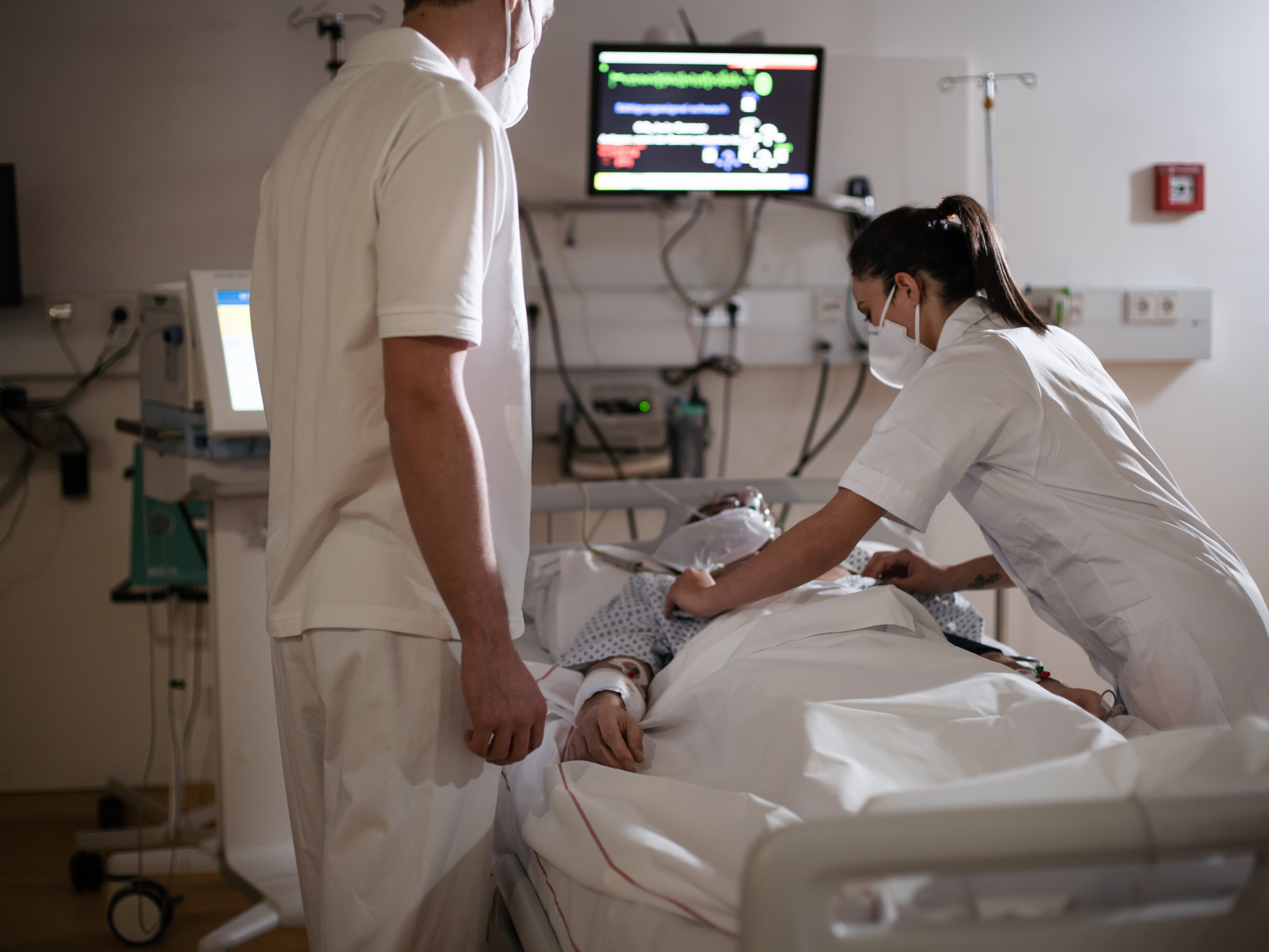 Bild von zwei Personen die eine kranke Person im Krankenbett versorgen.